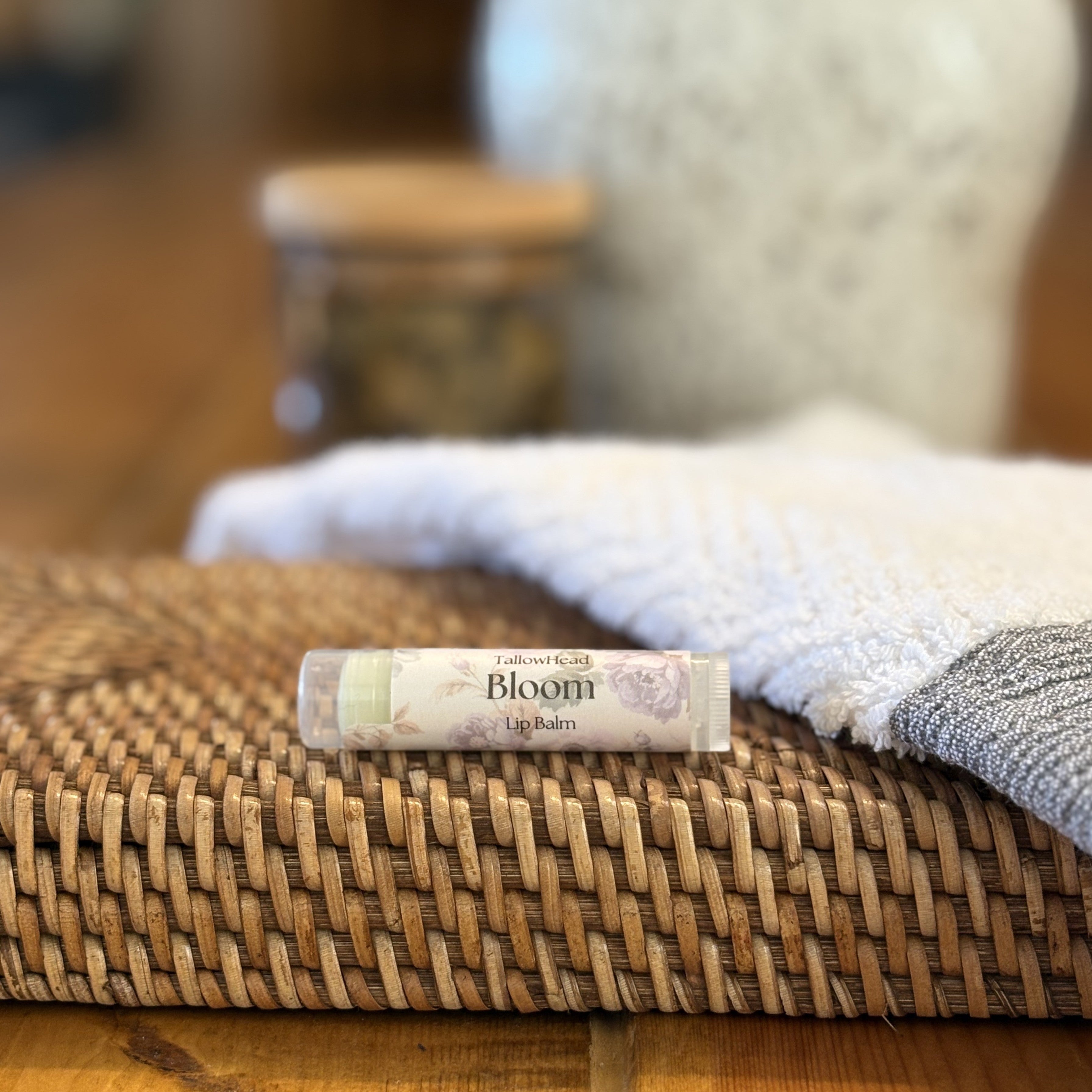 Balm tube labeled 'Bloom' on a woven mat with a blurred background