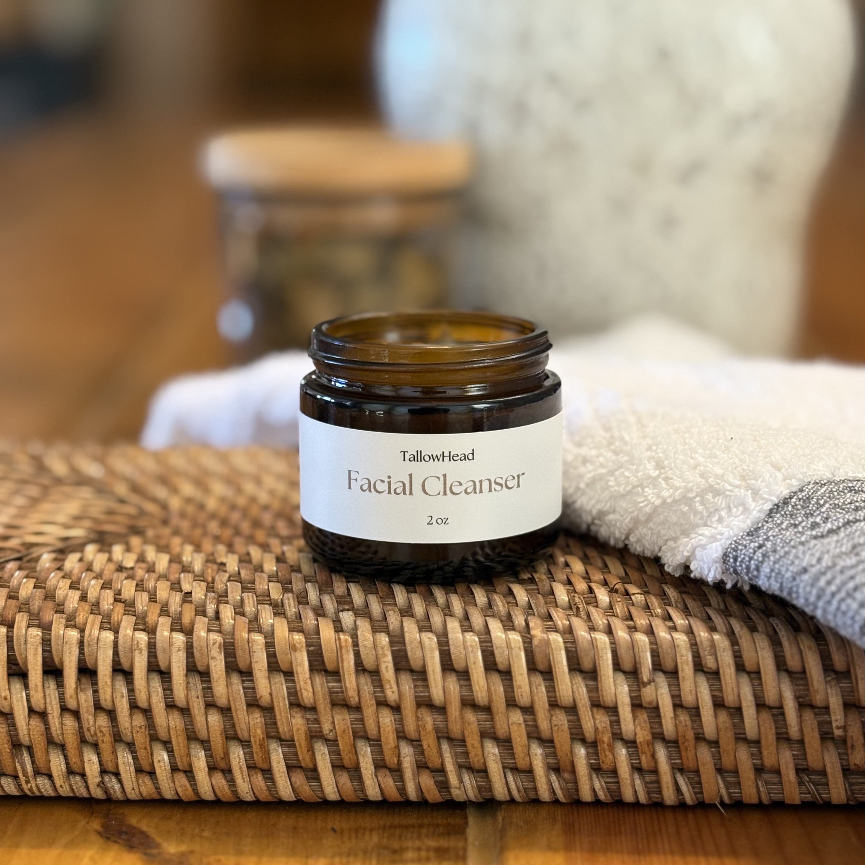 Facial cleanser jar on a woven mat with a blurred background