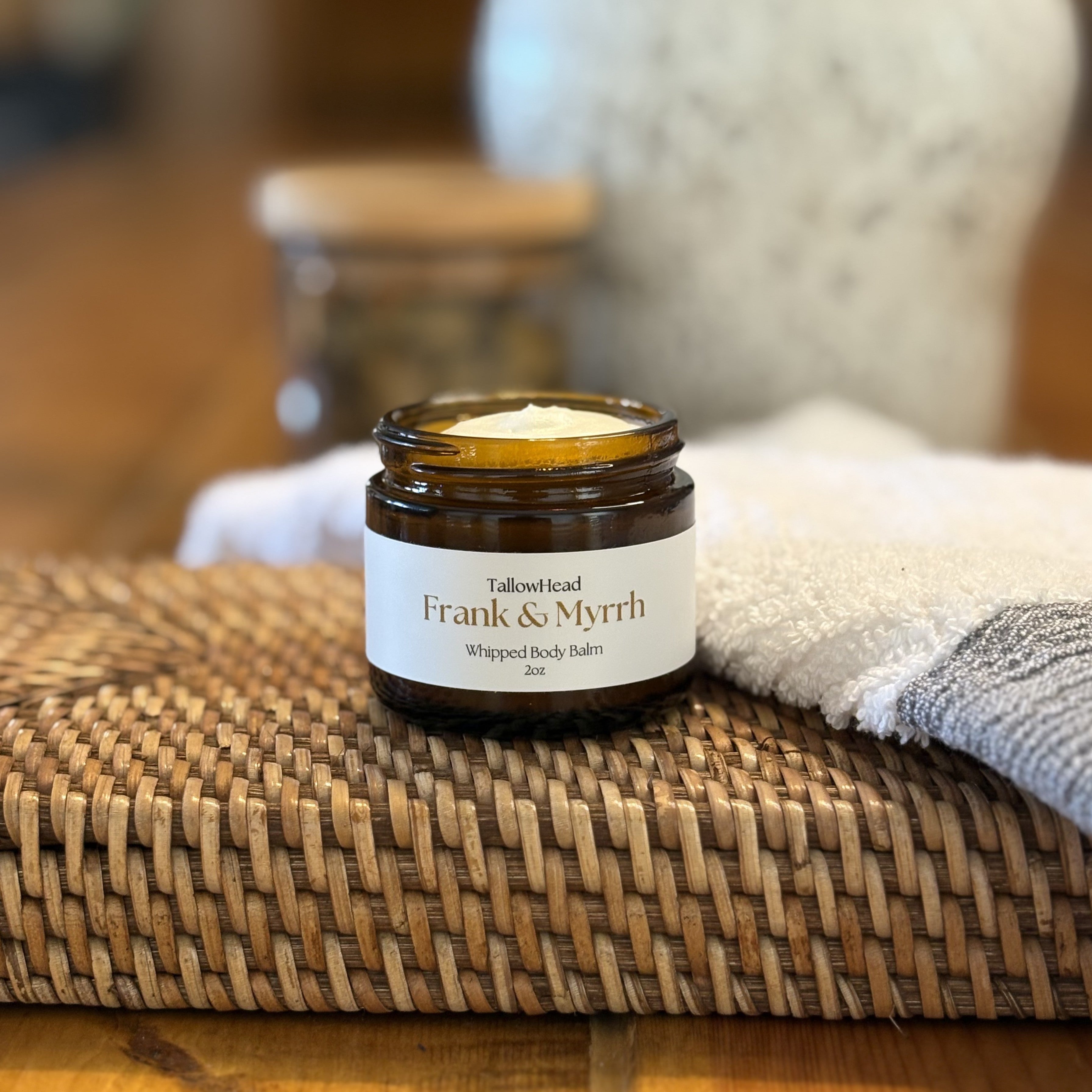 Jar of whipped body butter labeled 'Frank & Myrth' on a woven mat with a blurred background