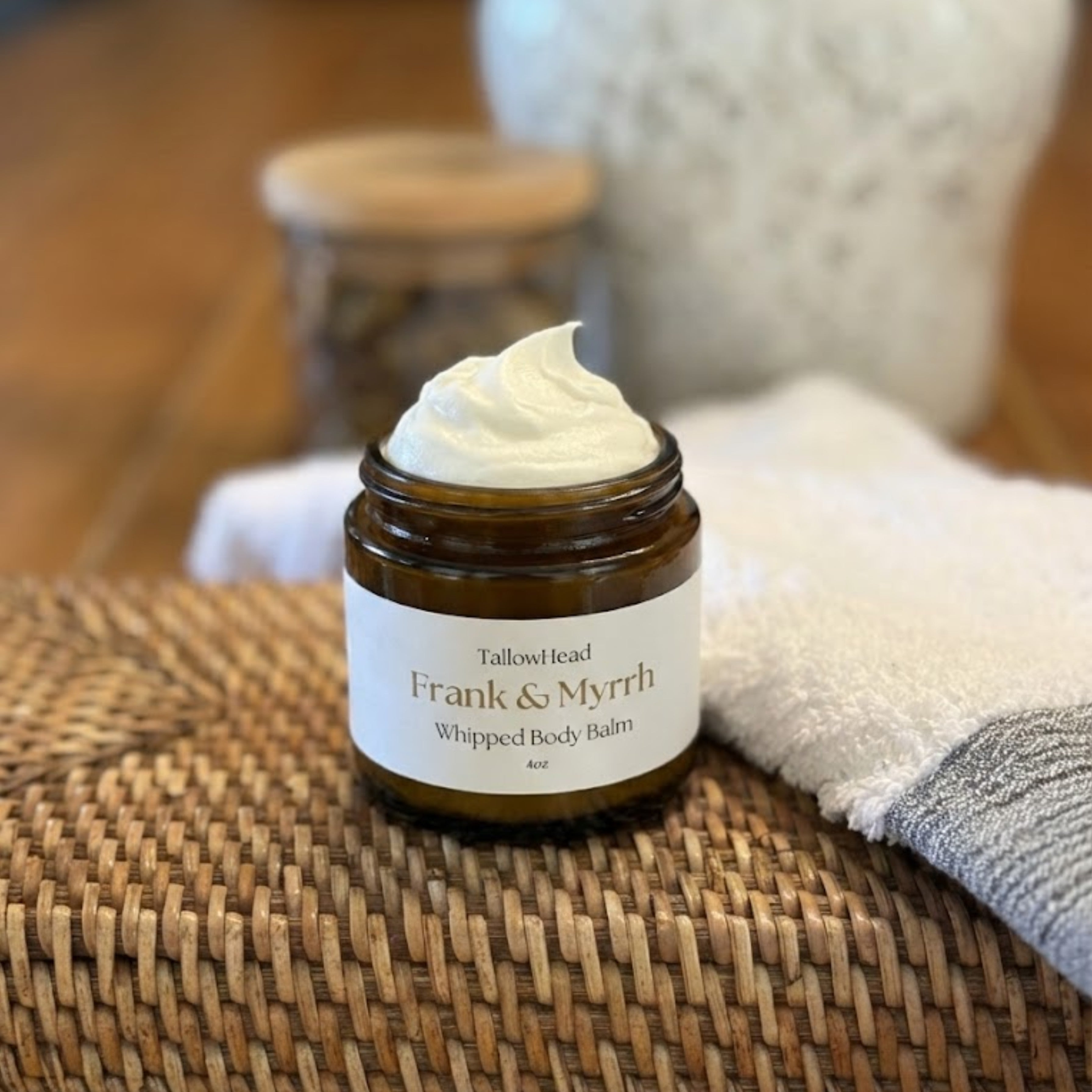 Jar of Frank & Myrrh whipped body balm on a woven mat with a blurred background