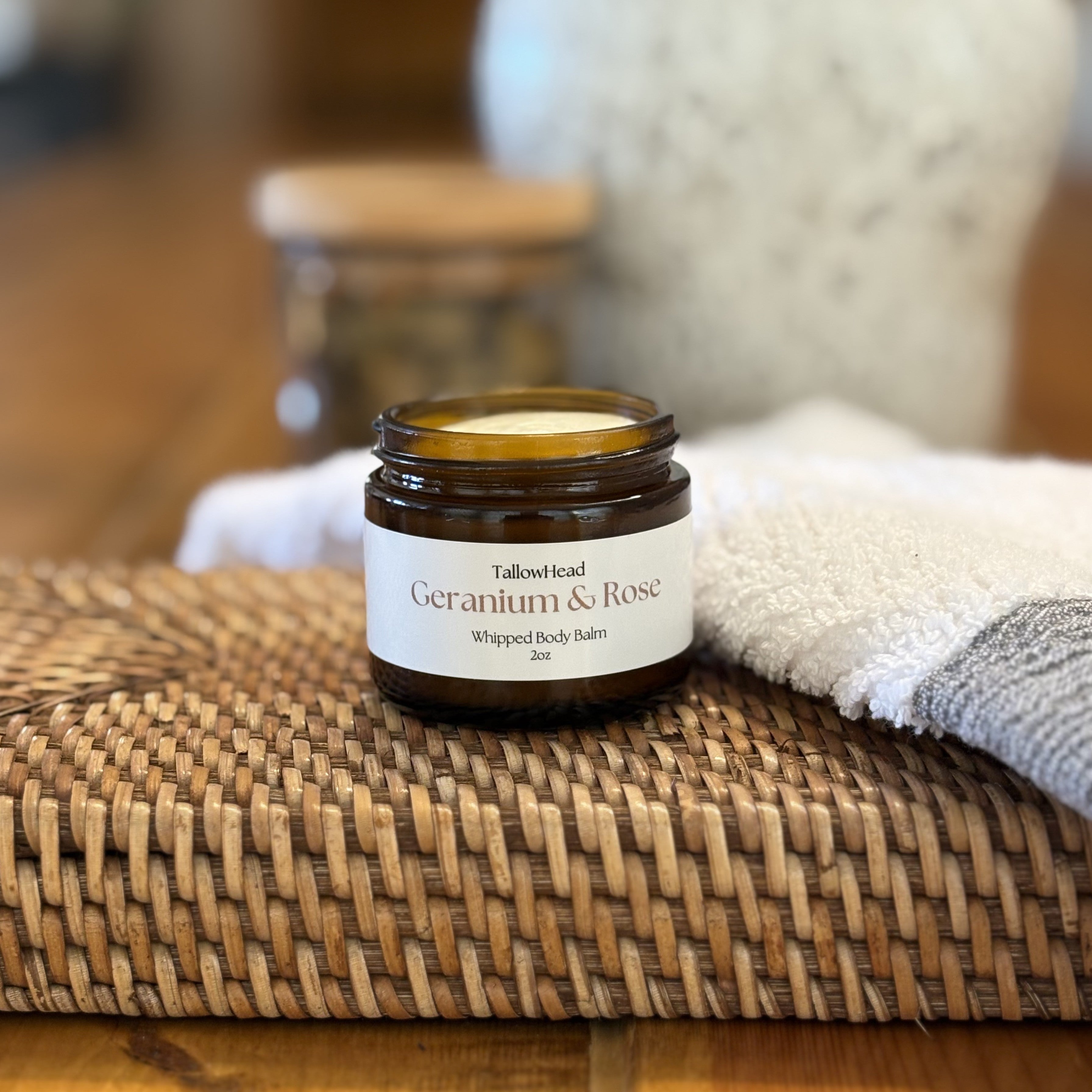 Jar of 'Geranium & Rose' whipped body balm on a woven mat with a blurred background