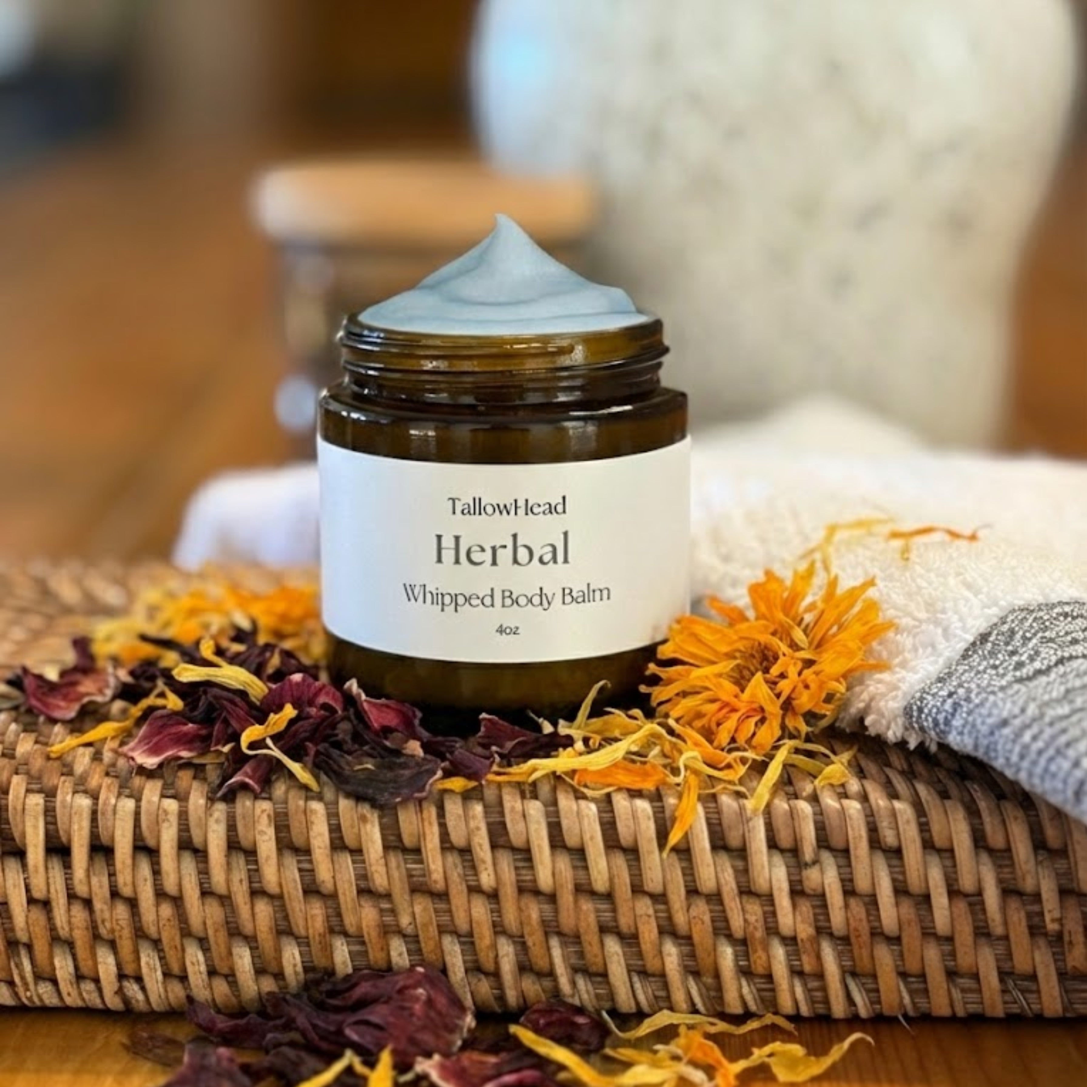 Herbal whipped body balm jar with dried flowers and a towel on a wooden surface