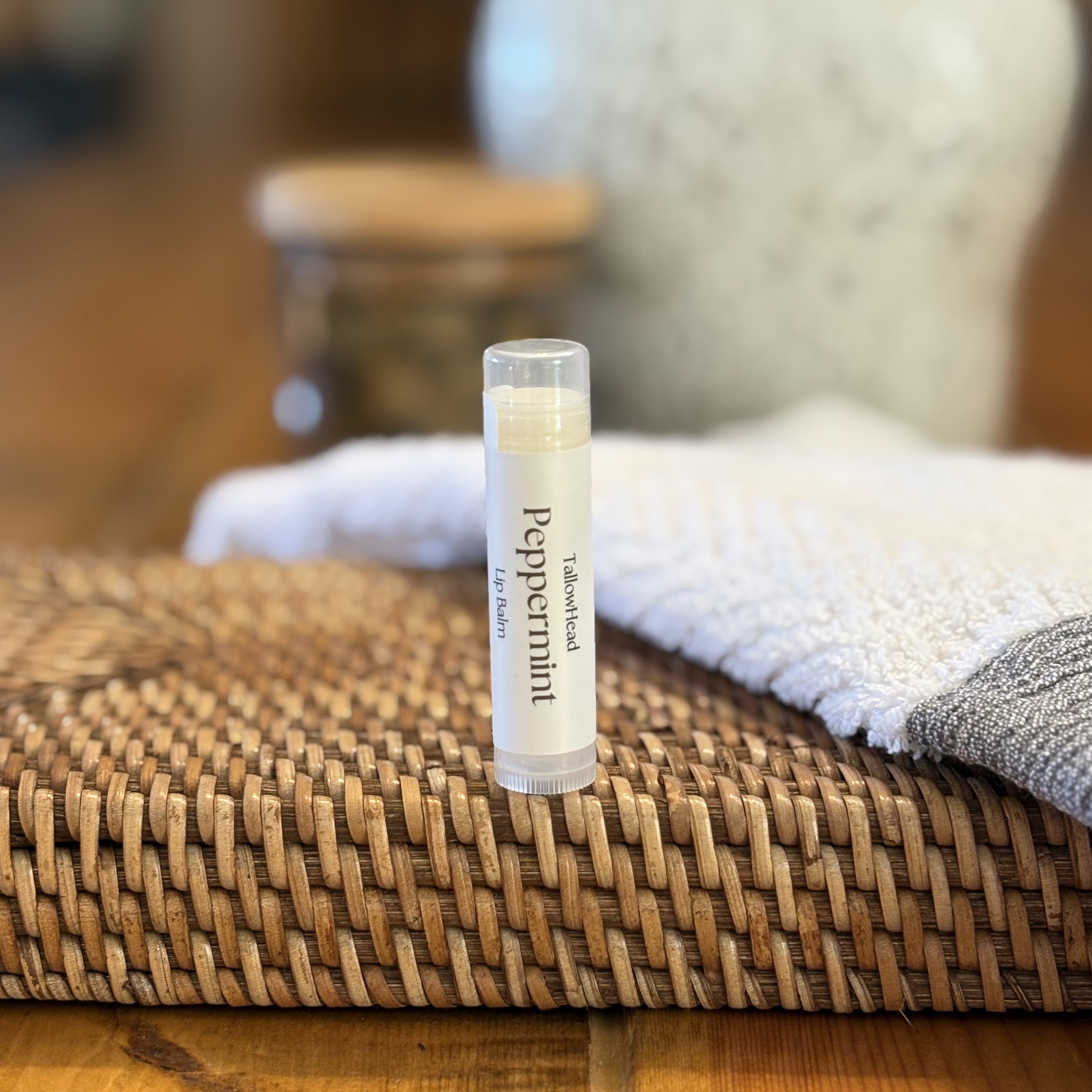 Lip balm tube labeled 'Peppermint' on a woven mat with a blurred background