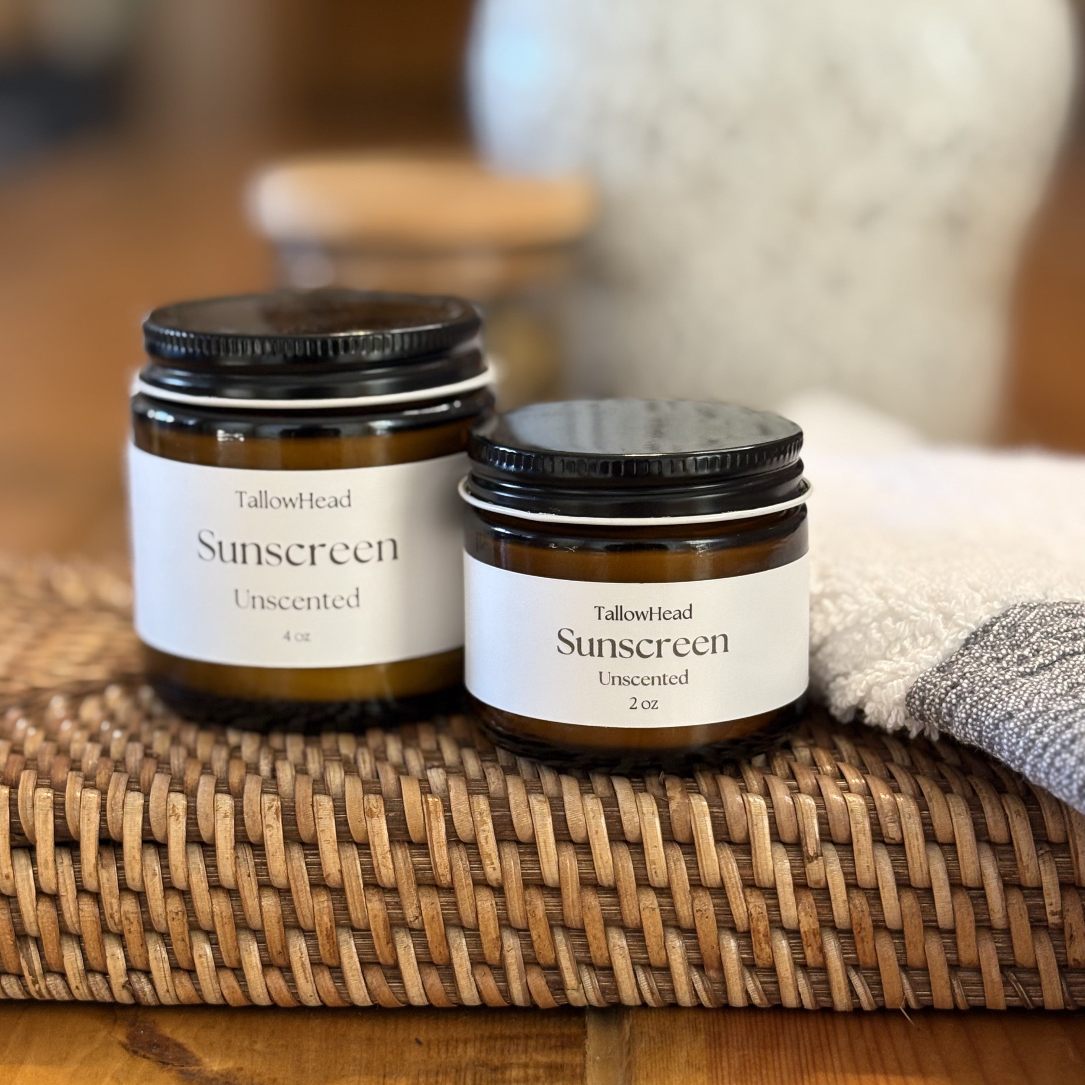 Two jars of TallowHead Sunscreen on a woven mat with a blurred background