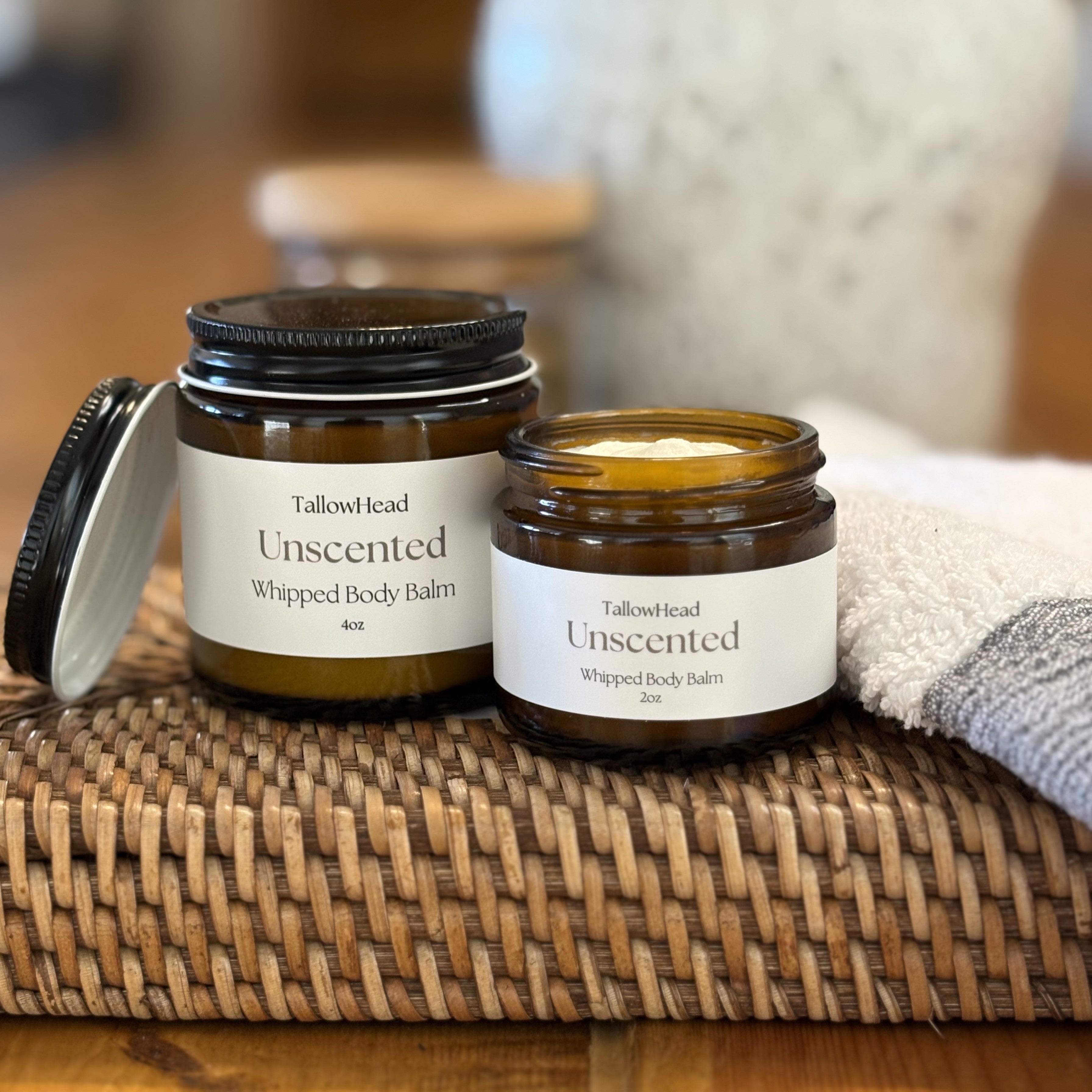 Two jars of TallowHead Unscented Whipped Body Balm on a woven mat with a blurred background.