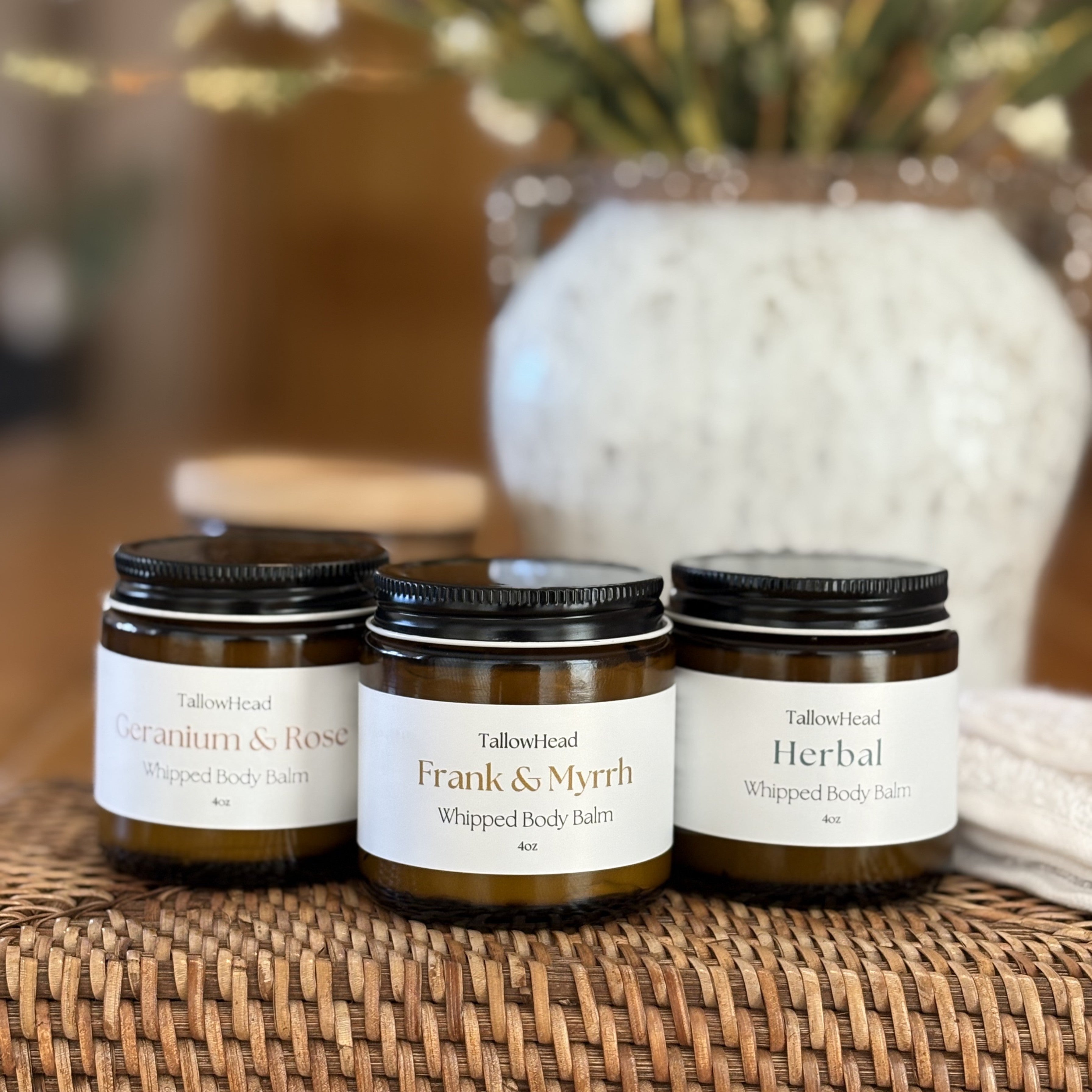 Three jars of Tallowhead body balms on a woven mat with a blurred background